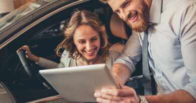 Schöne junge Frau unterhält sich mit dem gutaussehenden bärtigen Verkaufsleiter bei der Auswahl eines Autos im Autohaus. Der Mann benutzt ein digitales Tablet