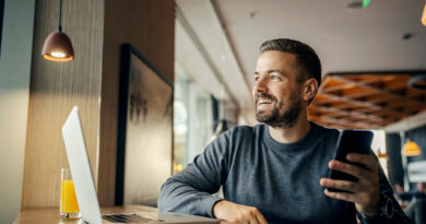 Ein glücklicher Freiberufler arbeitet in einem Café an sozialen Medien und nutzt dabei mehrere Technologien.